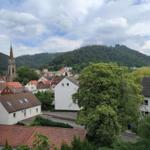 Panoramablick auf ein Dorf mit Kirche und bewaldeten Bergen im Hintergrund.