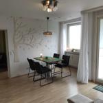 Essbereich mit Tisch, Stühlen und Wanddekoration. Durchgang zum Wohnzimmer. Terrasse über Glastür.