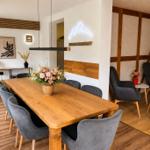 Esszimmer mit Holztisch, grauen Stühlen und Blumenarrangement. Wandgestaltung mit Holz und Neon.