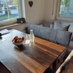 Holztisch mit Obstschale und Wasserflasche, graue Sitzbank und Fenster mit Blick.