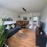 Wohnzimmer mit Sofa, Couchtisch und Essbereich. Holzfußboden und Blick in die Küche.