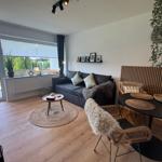 Wohnzimmer mit Sofa, Esstisch und Terrassentür. Holzboden und Pflanzen.