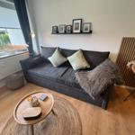 Ein Wohnzimmer mit grauem Sofa, Holzboden und runden Tisch.