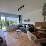Wohnbereich mit Sofa, Esstisch und Balkontür. Holzboden und Pflanzen.