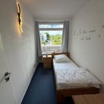 Ein Schlafzimmer mit Bett, Nachttisch und Fenster mit Blick nach draußen.