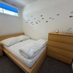 Schlafzimmer mit Bett, Kleiderschrank und Fenster mit blauen Jalousien.
