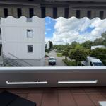 Balkon mit Blick auf Wohngebäude und grüne Umgebung unter blauem Himmel mit Wolken.