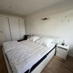Schlafzimmer mit weißem Bett, Nachttisch und Schrank. Holzfußboden und Wanddekoration.