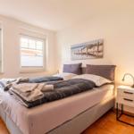 Bedroom with double bed, two windows, and nightstand with lamp.