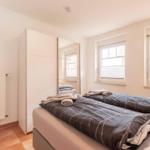Room with double bed, mirrored wardrobe, and two windows with blinds.