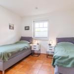 Two single beds with green bedspreads, nightstands, and windows with blinds.