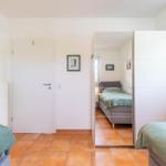 Room with two beds, mirrored wall, and window. Tile floor and white walls.