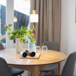 Runder Tisch mit Stühlen, Blumen und Fernglas. Fensterblick und Wandbild.