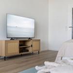 Schlafzimmer mit TV auf Holzregal und Bett mit weißer Bettwäsche.