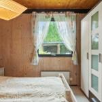 Schlafzimmer mit Holzwand, Bett, Kleiderschrank und Fenster mit Vorhängen.
