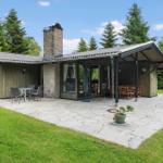 Haus mit Terrasse, Grillplatz und Garten. Holzverkleidung und Steinmauer sichtbar.