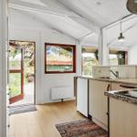 Küche mit Arbeitsfläche, Spüle und Fenster. Tür führt nach draußen.