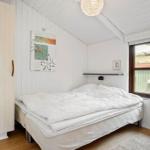 Schlafzimmer mit weißem Bett, Holzwand und Fensterblick auf Garten.