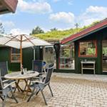 Terrasse mit Tisch, Stühlen und Sonnenschirm vor einem grünen Haus mit Dachgarten.