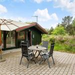 Terrasse mit Tisch, Stühlen und Sonnenschirm vor einem grünen Haus.