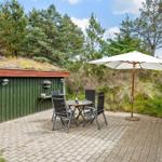 Terrasse mit Tisch, Stühlen und Sonnenschirm neben grünem Holzhaus und Wald.