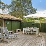 Terrasse mit Sonnenschirm, Tisch, Stühlen und Liegestühlen. Hintergrund: grüne Wand und Bäume.