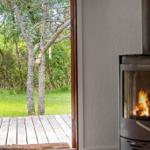 Holzofen mit brennendem Feuer, Blick auf grünen Garten und Holzterrasse.
