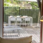 Terrasse mit Tisch, Stühlen und Sonnenschirm. Hintergrund: grüner Zaun und Garten.