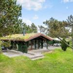 Grüne Hütte mit Terrasse, umgeben von Bäumen und Gras.