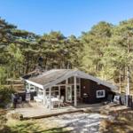 Moderne Hütte mit Holzterrasse und Grill im Wald. Weiße Möbel und große Fenster.