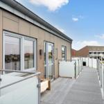 Außenbereich mit Glasgeländer und Zugang zur Wohnung. Hintergrund: Gebäude und Grünfläche.