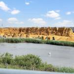Große Sandkunst an einem See mit Besuchern und Grünflächen im Hintergrund.