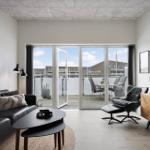 Wohnzimmer mit Sofa, Couchtisch und Sessel. Durchgehende Glastüren führen auf eine Terrasse.