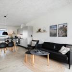 Wohn- und Essbereich mit schwarzer Couch, Tisch und Stühlen. Küche im Hintergrund.