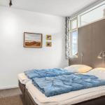 Schlafzimmer mit Doppelbett, Wandbildern und Fenster mit Vorhängen.