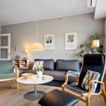 Wohnzimmer mit Sofa, zwei Stühlen und Tisch. Fenster, Pflanzen und Wandbilder.