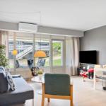 Wohn- und Essbereich mit Sofa, Stühlen und TV. Große Fenster mit Blick auf Außenbereich.