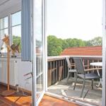 Terrasse mit Tisch und Stühlen, Blick auf Dach und Bäume. Fenster öffnet sich in Wohnraum mit Holzfußboden.