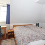 Ein Schlafzimmer mit Doppelbett, Schreibtisch, Lampe und Fenster mit Vorhang.