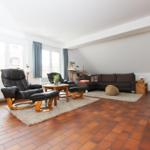 Wohnzimmer mit Sofa, Sessel und Holzmöbel. Terrakottaboden und große Fenster.