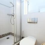 Dusche mit Duschbrause, Toilette und WC-Behälter an der Wand.
