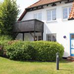 Wohnhaus mit Balkon, grünem Garten und blauer Tür mit Blumenmotiv.