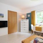 Ein Raum mit Fernseher, Schrank, Tisch und Fenster mit gelben Vorhängen.