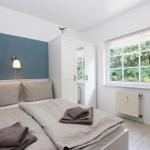 Schlafzimmer mit Bett, Kleiderschrank und Fenster mit Blick auf Bäume.