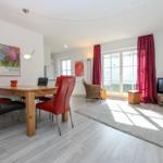 Essbereich mit Tisch und Stühlen, Wohnbereich mit Fernseher und Fenster mit roten Vorhängen.