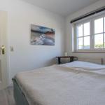 Schlafzimmer mit Bett, Fenster und Wandbild. Tür links, Tisch rechts.
