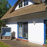 Haus mit strohgedecktem Dach, blauen Fensterrahmen und Strandkorb im Vorgarten.