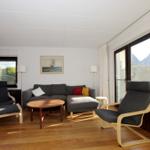 Wohnzimmer mit Sofa, zwei Sesseln, Tisch und großen Fenstern.