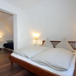 Schlafzimmer mit Doppelbett, Nachttischen und Lampen. Durchgang zum angrenzenden Raum.