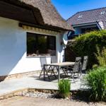 Haus mit Dach und Terrasse mit Tisch und Stühlen. Hinterhof mit Hecke und Pflanzen.